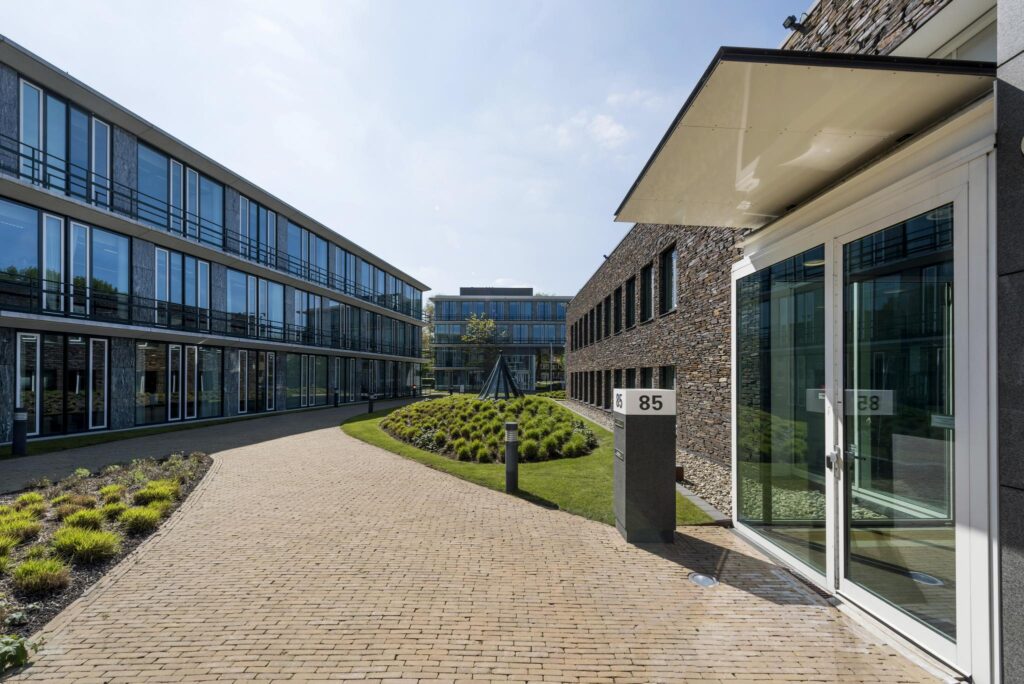 Modern kantoorgebouw aan de De Cuserstraat 85 met glazen gevels en een verzorgde binnentuin.